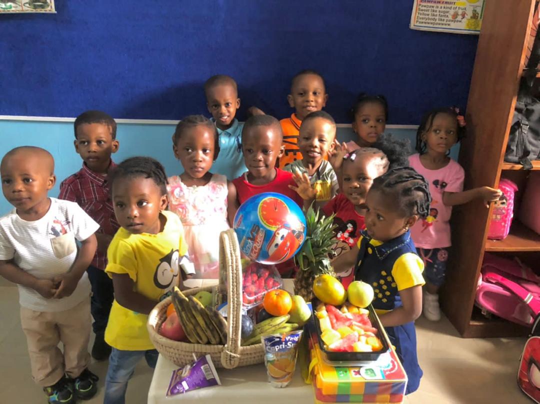 ACES nursery children gathered around a basket of fresh fruit on Fruit Day